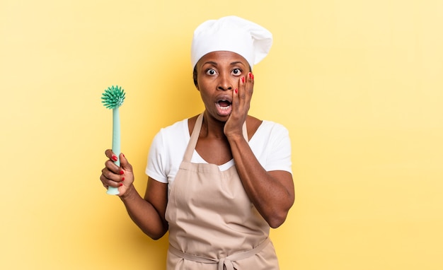 Zwarte afro-chef-vrouw voelt zich geschokt en bang, ziet er doodsbang uit met open mond en handen op de wangen. afwas concept