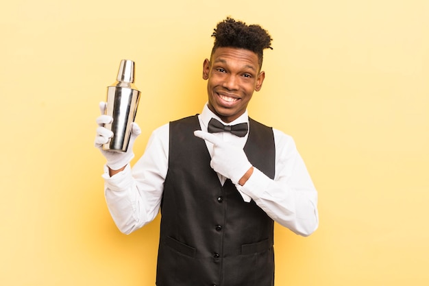 Zwarte afro jonge man die vrolijk glimlacht en zich gelukkig voelt en naar de zijbarman en het cocktailconcept wijst