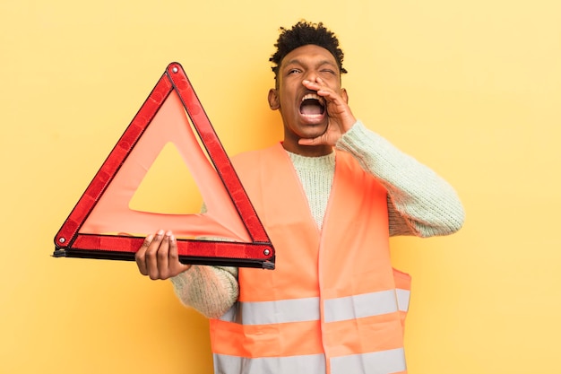 Zwarte afro jonge man voelt zich gelukkig en geeft een grote schreeuw met handen naast mond autofout en driehoeksconcept