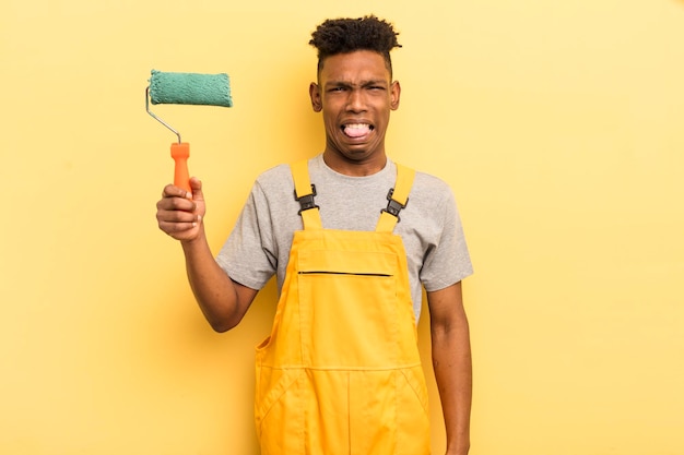 Zwarte afro jonge man voelt zich walgelijk en geïrriteerd en tong uit huishoudster die naar huis schildert