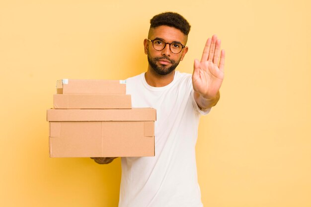 Zwarte afro-man die er serieus uitziet en open palm laat zien die een stopgebaar verzenddozenconcept maakt