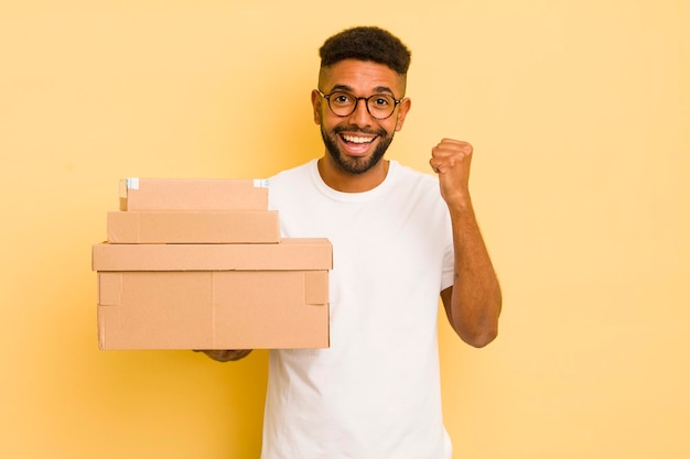 Zwarte afro-man die geschokt is, lacht en viert succes met het concept van verzenddozen