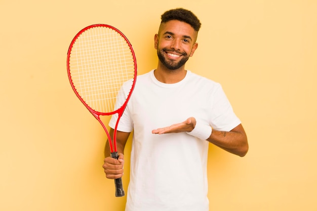 Zwarte afro-man die vrolijk lacht en zich gelukkig voelt en een concept tennisconcept toont