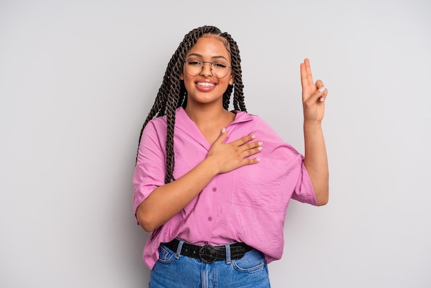 Zwarte afro-vrouw die er gelukkig zelfverzekerd en betrouwbaar uitziet, glimlacht en een overwinningsteken toont met een positieve houding