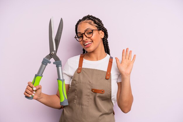 Zwarte afro-vrouw die vrolijk lacht, met de hand zwaait, je verwelkomt en begroet. tuinman of boer concept