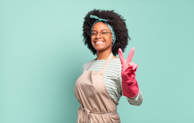 Zwarte afrovrouw die gelukkig, zorgeloos en positief glimlacht en kijkt, met één hand overwinning of vrede gebaart.