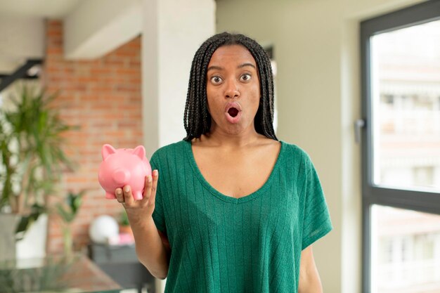 Foto zwarte afrovrouw voelt zich extreem geschokt en verrast spaarvarkenconcept