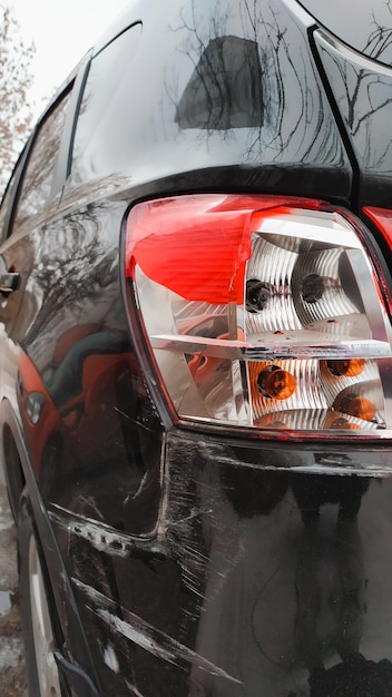 Zwarte auto na een ongeval bekrast bumper gebroken koplamp Achteraanzicht close-up verticaal