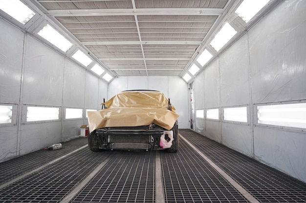 Foto zwarte auto staat in cabine met felle verlichting om te schilderen bedekt met speciale doek en klaar voor reparatie