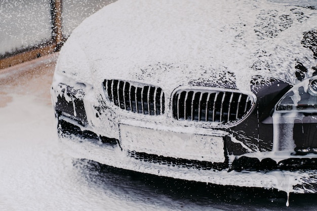 Zwarte auto wordt gewassen met zeep autowasconcept auto bij carwash gewassen met waterstraalspray voertuig in schuim