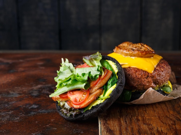 Zwarte broodjeshamburger op de ruimte van het houten dienbladexemplaar. Open cheeseburger met kotelet en groenten, snel voedselconcept