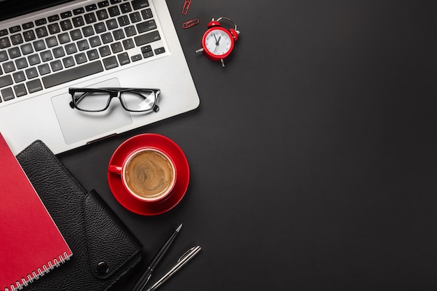 Zwarte bureautafel met leeg scherm laptopcomputer, wekker, notebook, kopje koffie en ander kantoor. Bovenaanzicht met kopieerruimte.