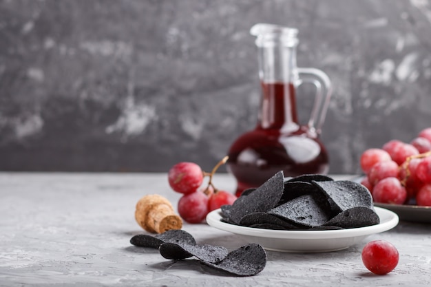 Zwarte chips met houtskool, balsamico azijn in glas, rode druiven op een blauwe keramische plaat