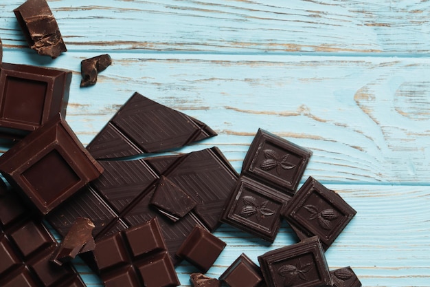 Zwarte chocolade verschillende stukken en een reep op een blauwe houten achtergrond. Bovenaanzicht. Plaats voor tekst.