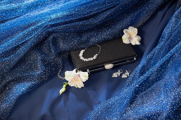 Zwarte clutch met sieraden op blauwe achtergronddoek