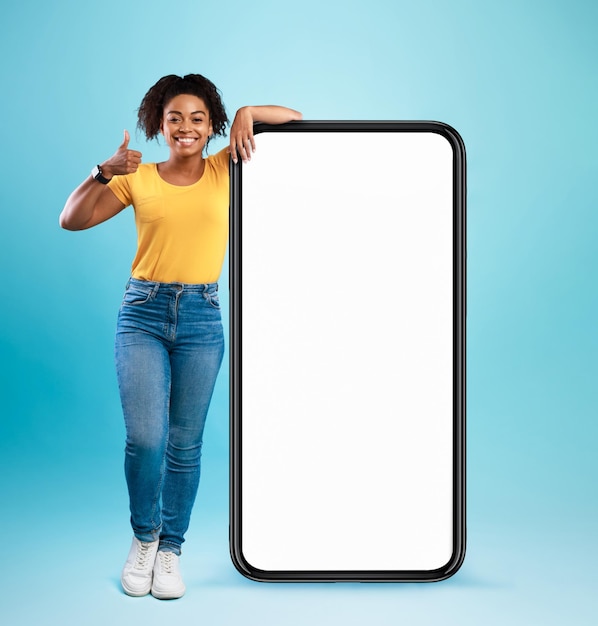 Zwarte dame leunt op haar mobiele telefoon met een leeg wit scherm en toont duim omhoog en beveelt een coole nieuwe app of website mockup aan