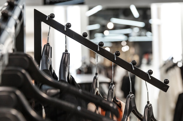 Zwarte diagonale standaard met zwarte plastic hangers met kleding in een winkel