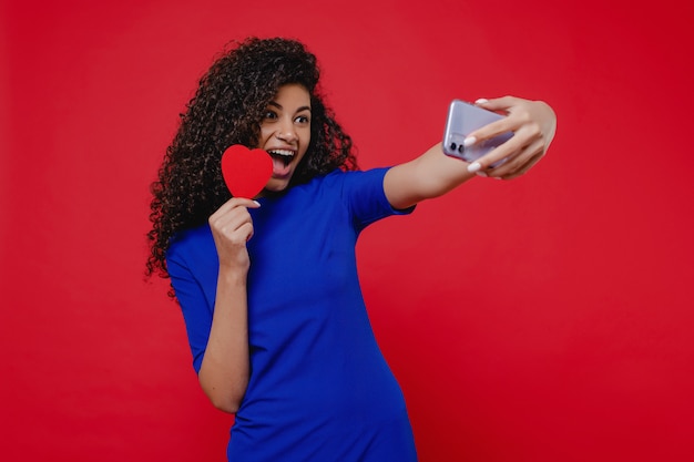 Zwarte die en selfie met hart gevormde valentijnskaartkaart glimlachen maken op rode muur