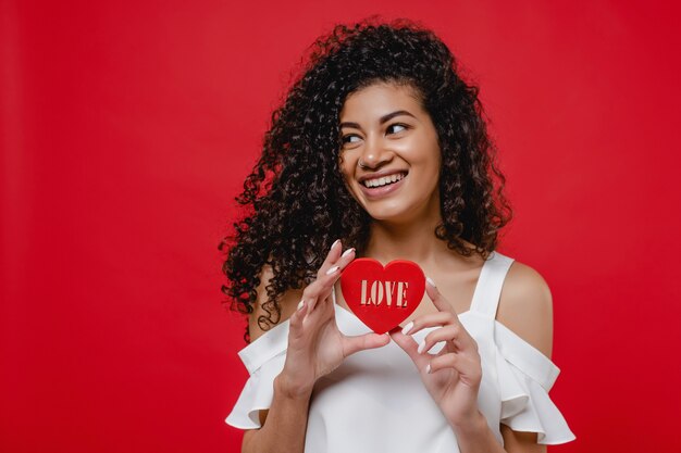 Zwarte die met het cijfer van de hartvorm met liefdesbrieven glimlacht op rode muur