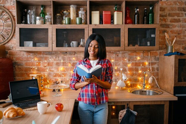 Zwarte die op zoek is naar receptenboek, jong etnisch meisje dat op de keuken kookt. Afrikaanse vrouwelijke persoon voorbereiding van plantaardige salade thuis, gezonde levensstijl