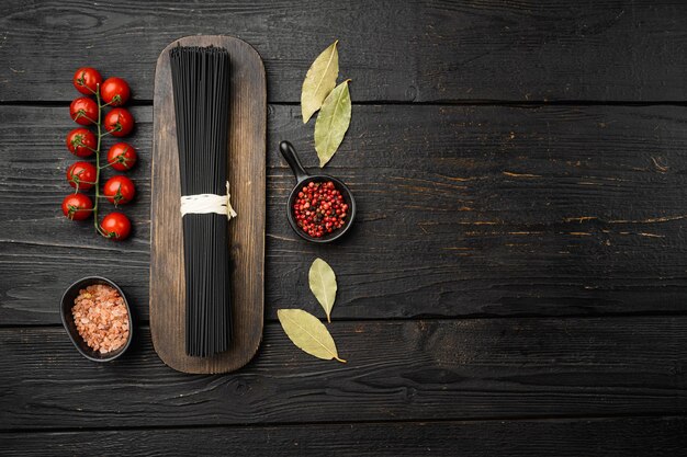 Zwarte droge rauwe noedels spaghetti pasta set, op zwarte houten tafel achtergrond, bovenaanzicht plat lag, met kopieerruimte voor tekst