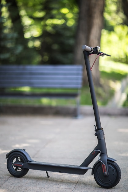 Zwarte elektrische scooter op bankachtergrond in het park elektrisch stadsvervoer op zonnige dag