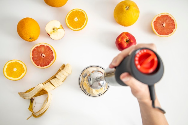 Zwarte elektrische staafmixer en accessoires met gesneden fruit op een witte achtergrond Bovenaanzicht plat lag