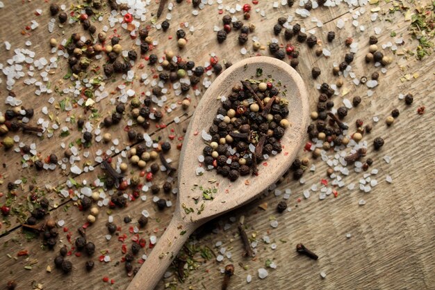 Zwarte en witte peper erwten zeezout kruidnagel kruiden in een lepel op een houten achtergrond