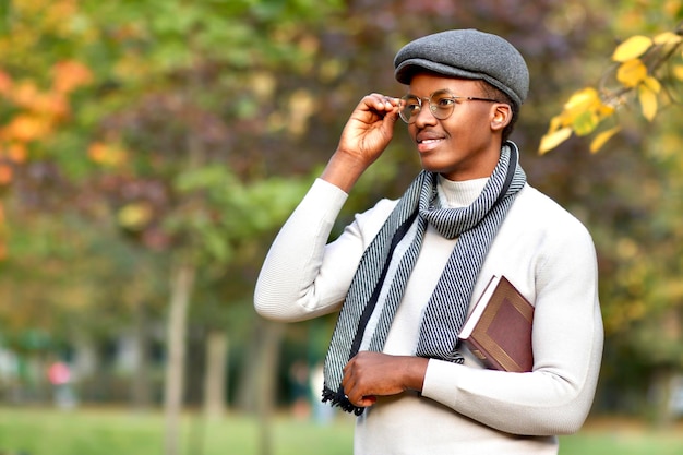 Zwarte gelukkige Afrikaanse Afro-Amerikaanse etnische student met boek bij het wandelen in het gouden herfstpark