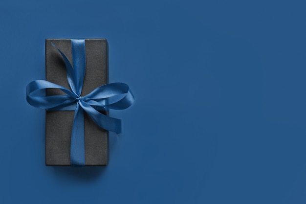 Zwarte geschenkdoos omwikkeld met blauw lint op klassiek blauw oppervlak.