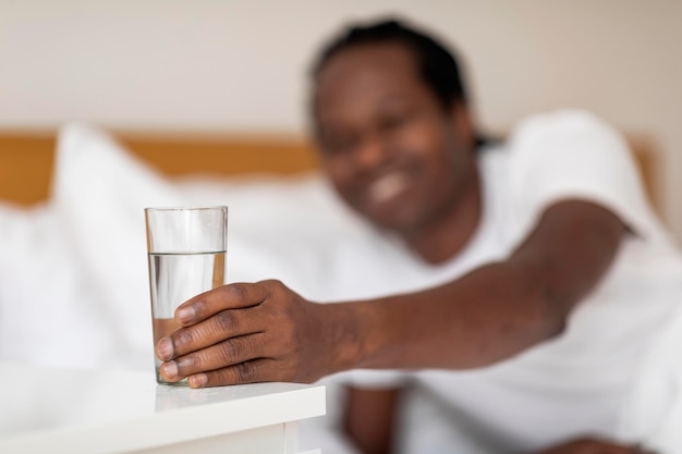 Zwarte glimlachende man die 's ochtends glas met water van het nachtkastje neemt