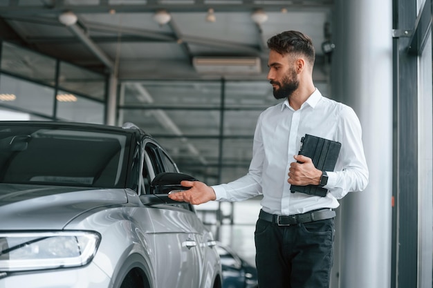 Zwarte grafische tablet in handen Jonge man in witte kleren is in de autodealer