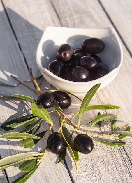 Zwarte Griekse olijven in een bord en op een groene tak op een houten tafel in Griekenland