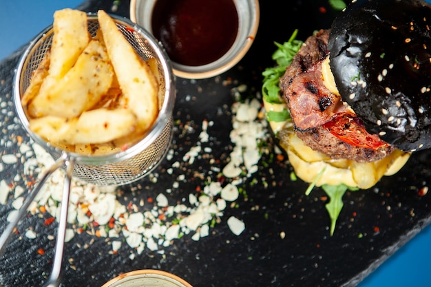 Zwarte hamburger met sappige rundvleespasteitje, kaas, frietjes. Trendy eten