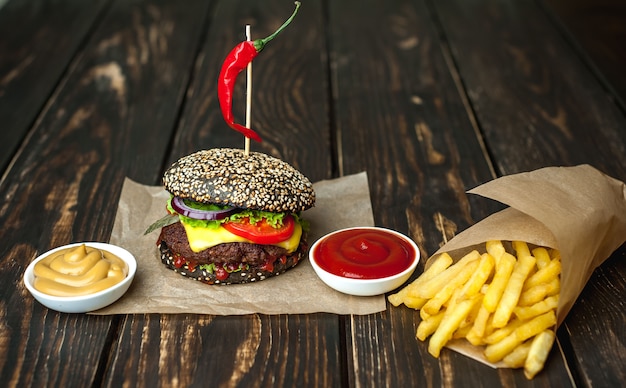 zwarte hamburger met sla, tomaten en frietjes. Houten achtergrond