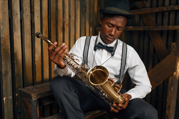 Zwarte jazzmuzikant zit met saxofoon. Zwarte jazzman in hoed poseert met instrument