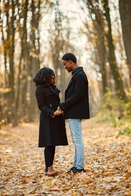 Zwarte jonge man en zijn vriendin hand in hand. Romantisch paar wandelen in herfst park. Man en vrouw die zwarte jassen dragen.