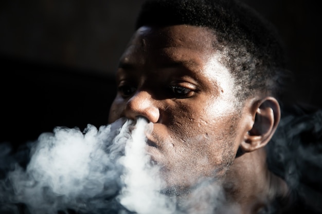 zwarte jonge man roken uit zijn neus zittend in een donkere kamer