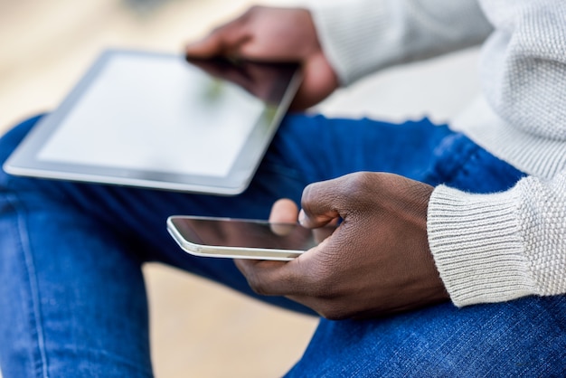 Zwarte jonge mensenhanden die tabletcomputer en smartphone houden