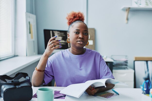 Zwarte jonge vrouw als creatieve ontwerper die paarse outfit draagt op de werkplek