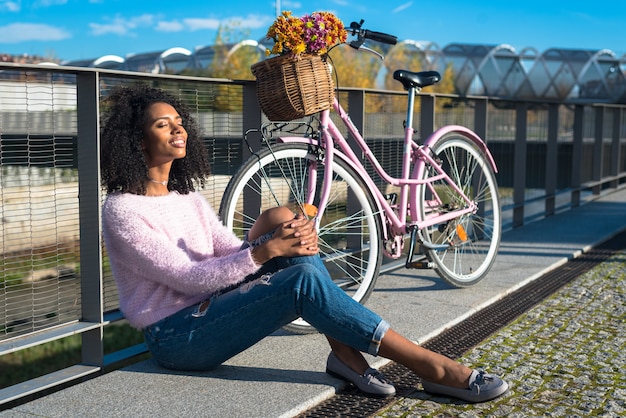 Zwarte jonge vrouwenzitting door de rivier met haar uitstekende fiets