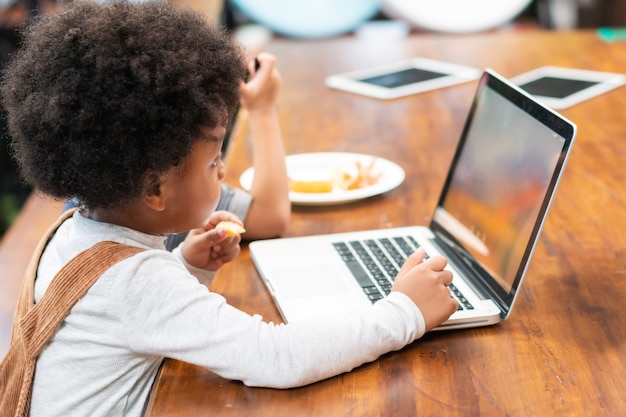 zwarte jongen computer spelen aan de eetkamer, leren en onderwijs