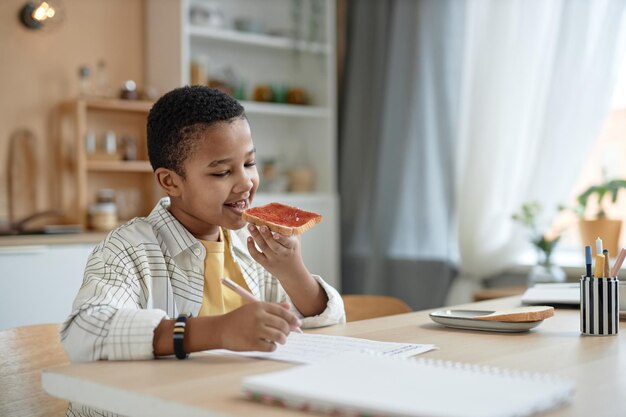 Zwarte jongen doet huiswerk aan de keukentafel.