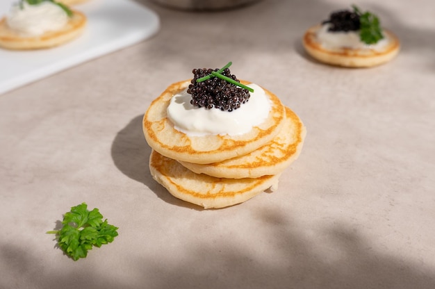 Zwarte kaviaar met zure room op een stapel mini blinis of pannenkoeken