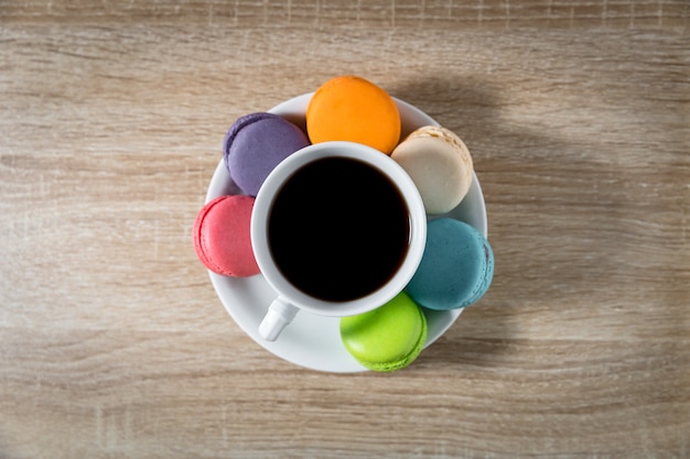 Foto zwarte koffie in een kopje met macarons op witte schotel op houten tafel achtergrond