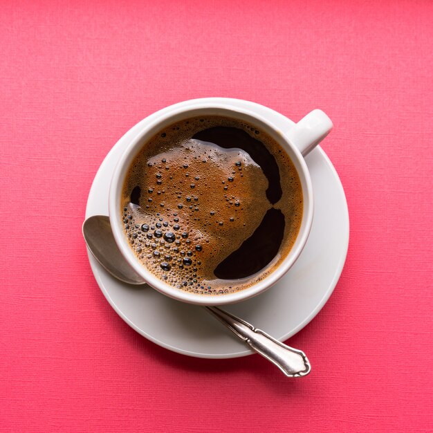 Zwarte koffie met schuim in een witte kop op blauwe achtergrond, plat gelegd.