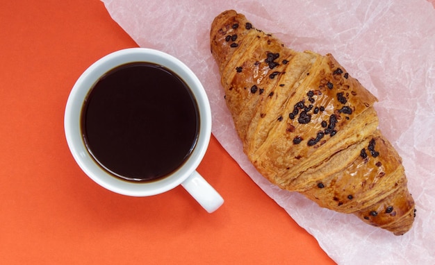 Zwarte koffie zonder melk in een witte kop en een chocoladecroissant op perkament en lichte achtergrond. Frans ontbijt met vers gebak. Bovenaanzicht plat met kopieerruimte voor uw tekst.