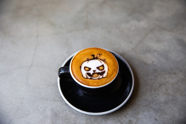 Zwarte kop cappuccinokoffie met latte art van halloween-symboolpompoen van kaneel op melkschuim