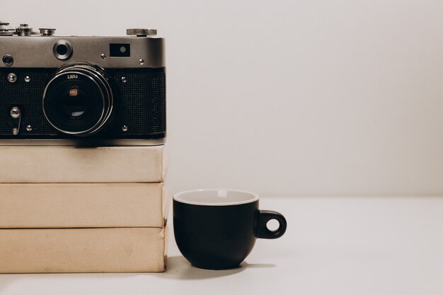 Zwarte kopje koffie met oude vintage camera en witte boeken