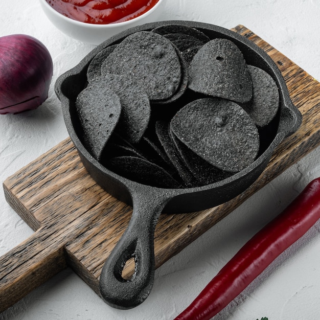 Zwarte krokante chips set, in gietijzeren koekenpan, op wit stenen oppervlak